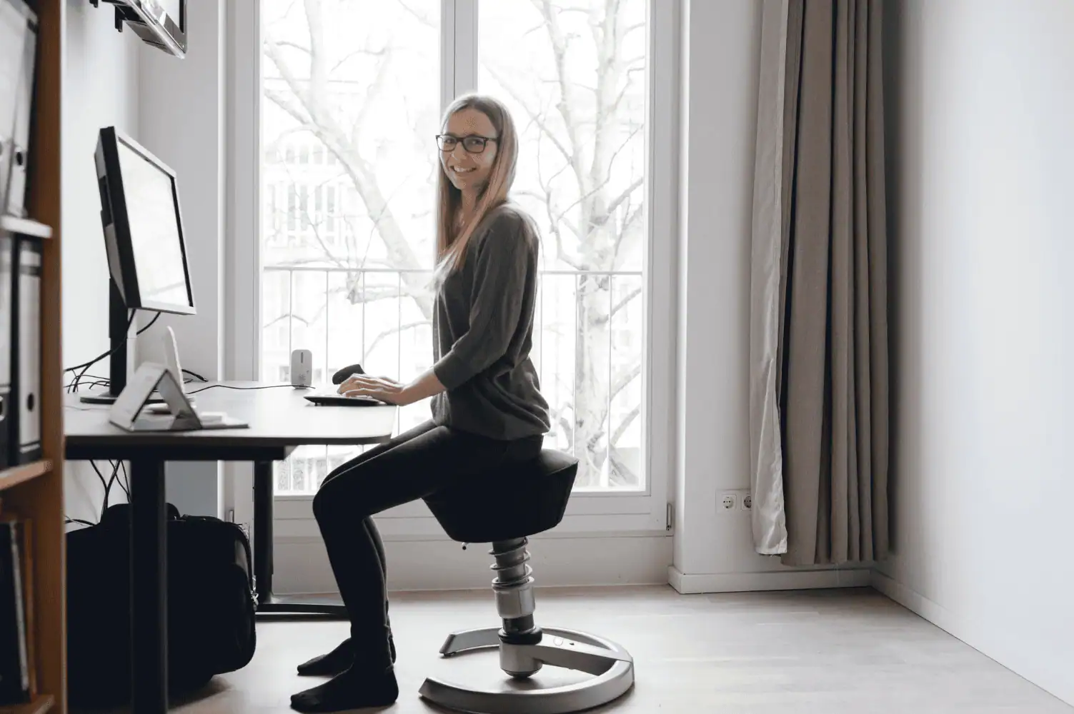 Eine Frau sitzt auf einem ergonomischen Stuhl vor einem Schreibtisch.
