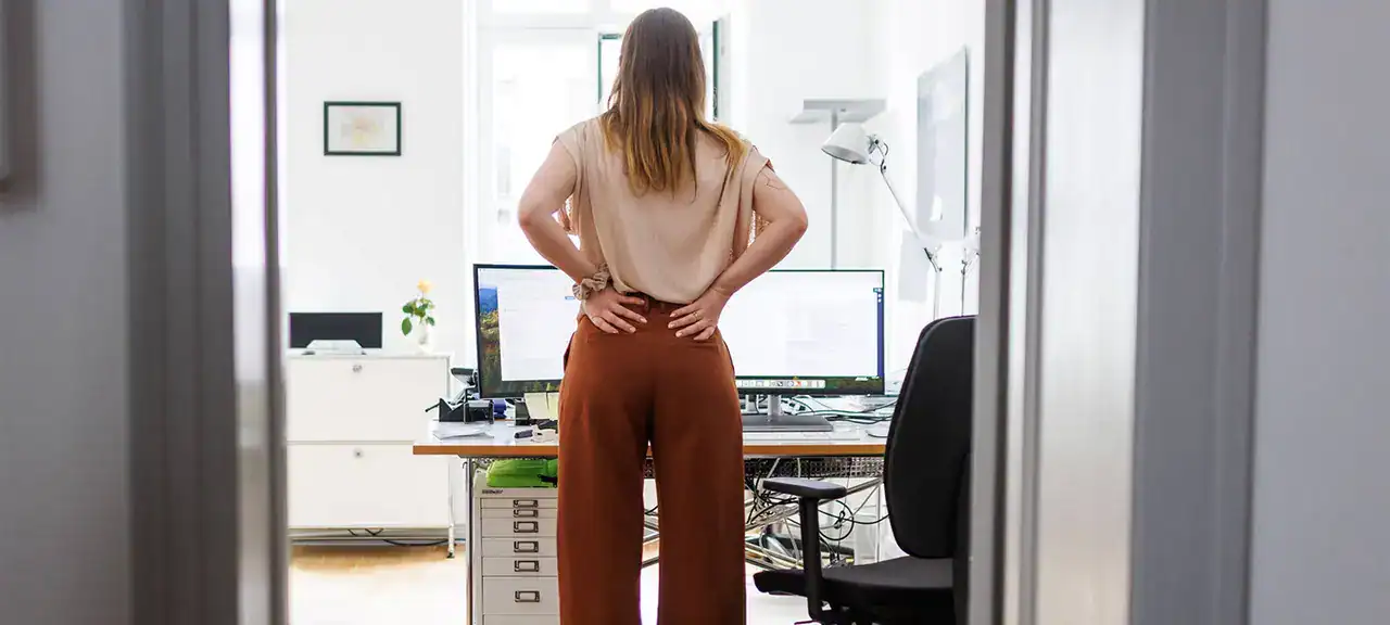 Eine Frau mit Rückenschmerzen steht in einem Büro.
